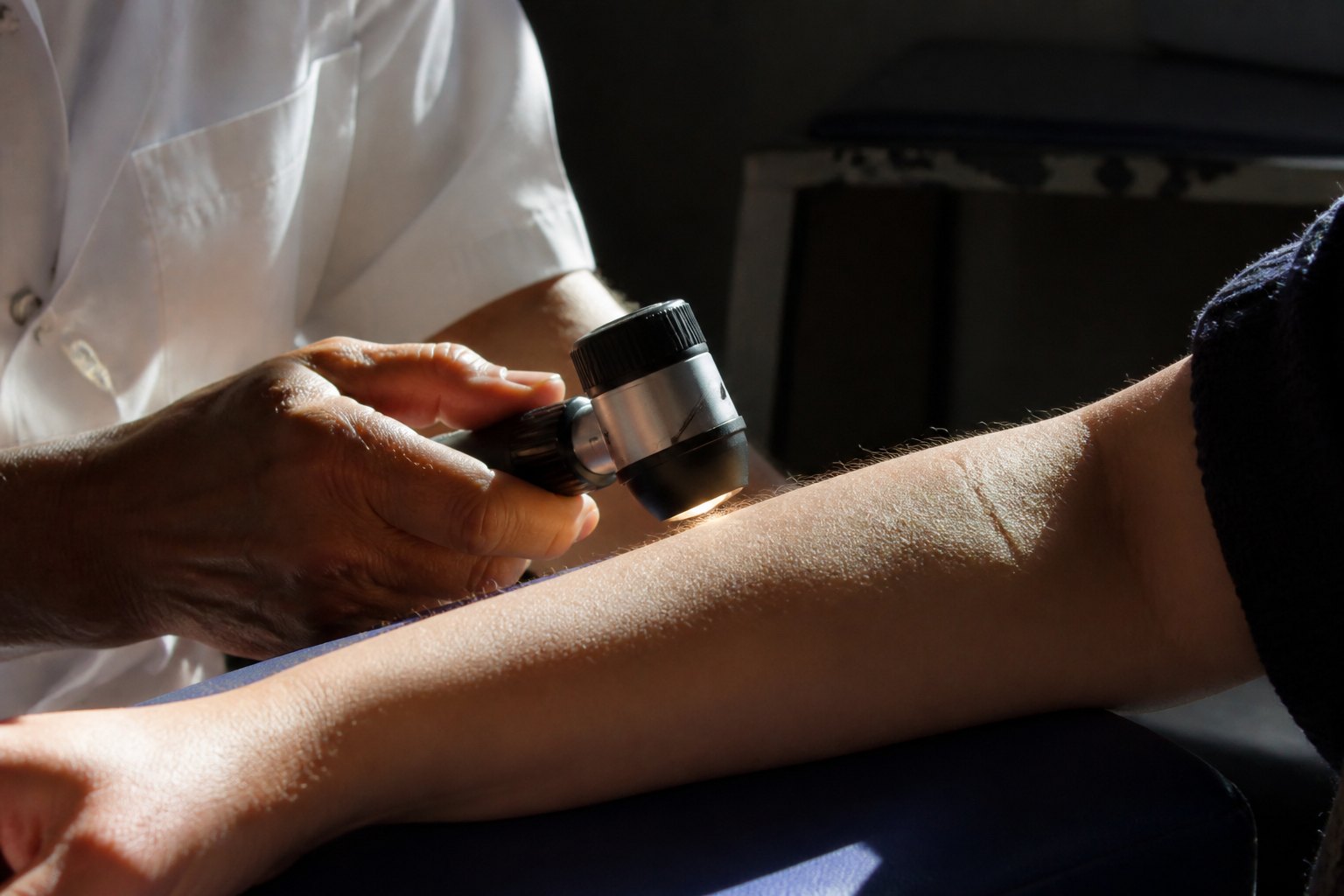 Clinician using a dermatoscope to examine a patient's arm during a skin check